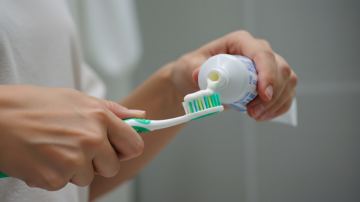 Hände eines Mannes drücken Zahnpasta aus der Tube auf eine Zahnbürste